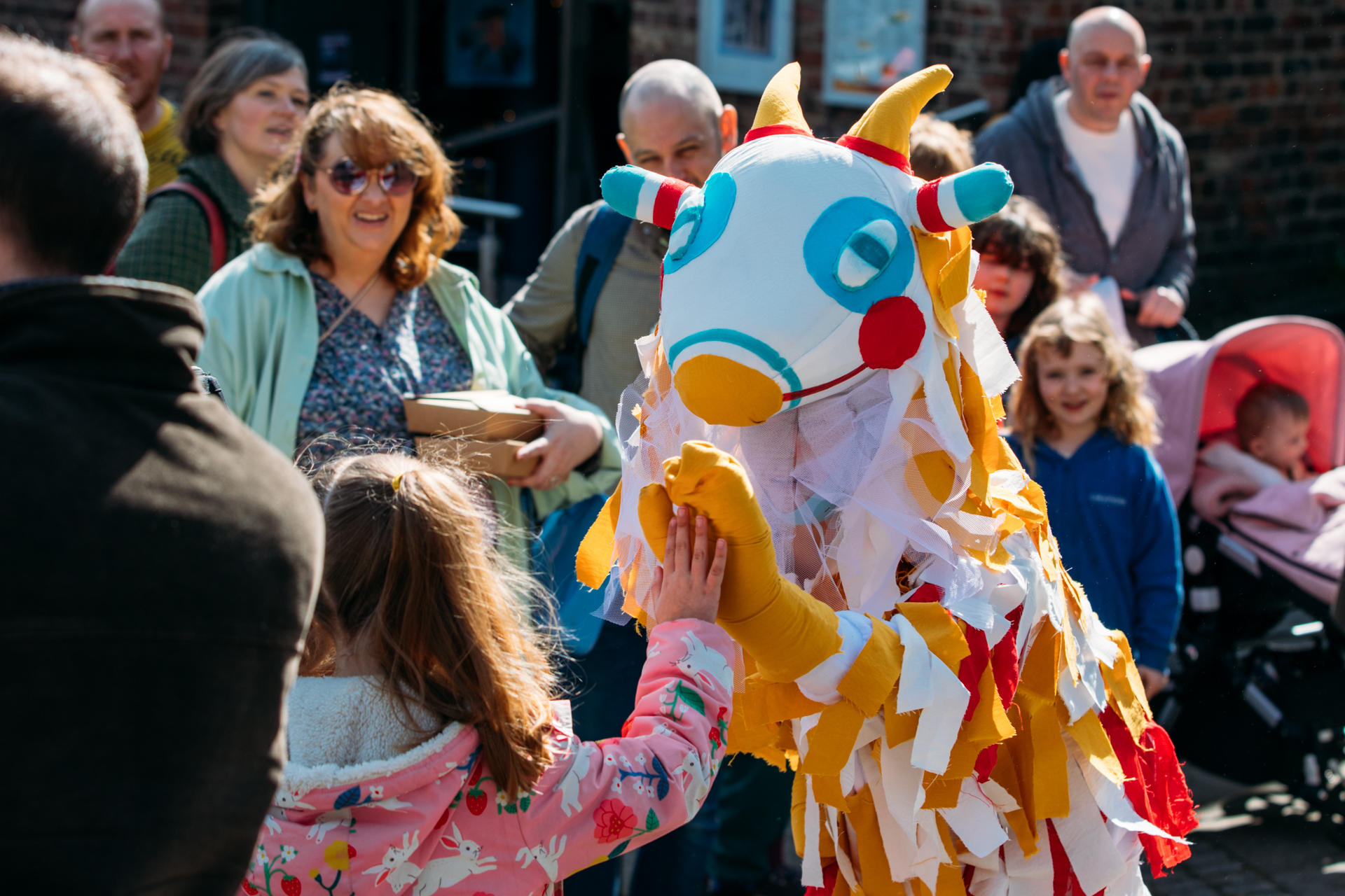 A colorful, handcrafted monster character interacts with a crowd during an outdoor festival.