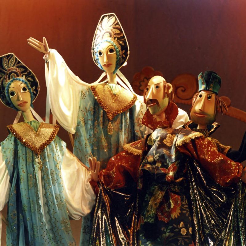 Elaborately dressed marionette puppets posed on a stage, with detailed costumes and expressive faces.