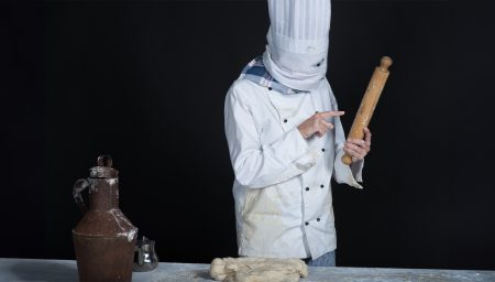 Person in chef costume with bread dough on table, holding rolling pin