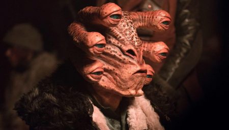 Close-up of a pinkish-orange alien with multiple eyes on thick stalks emerging from its head, wearing a dark fur-trimmed collar.