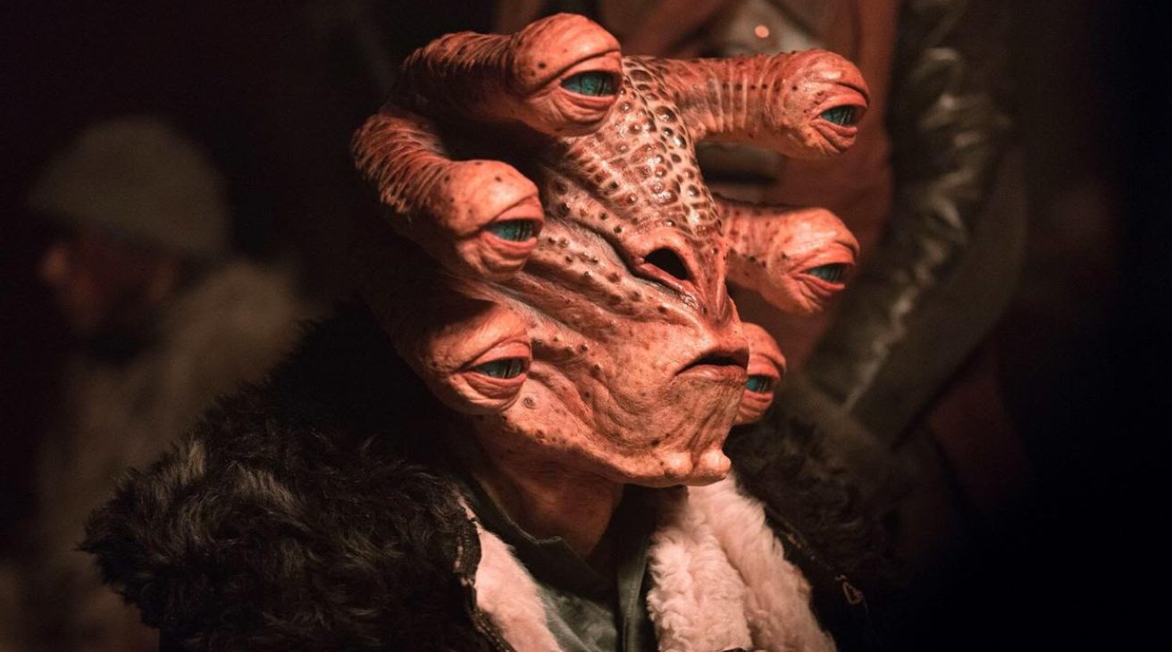Close-up of a pinkish-orange alien with multiple eyes on thick stalks emerging from its head, wearing a dark fur-trimmed collar.