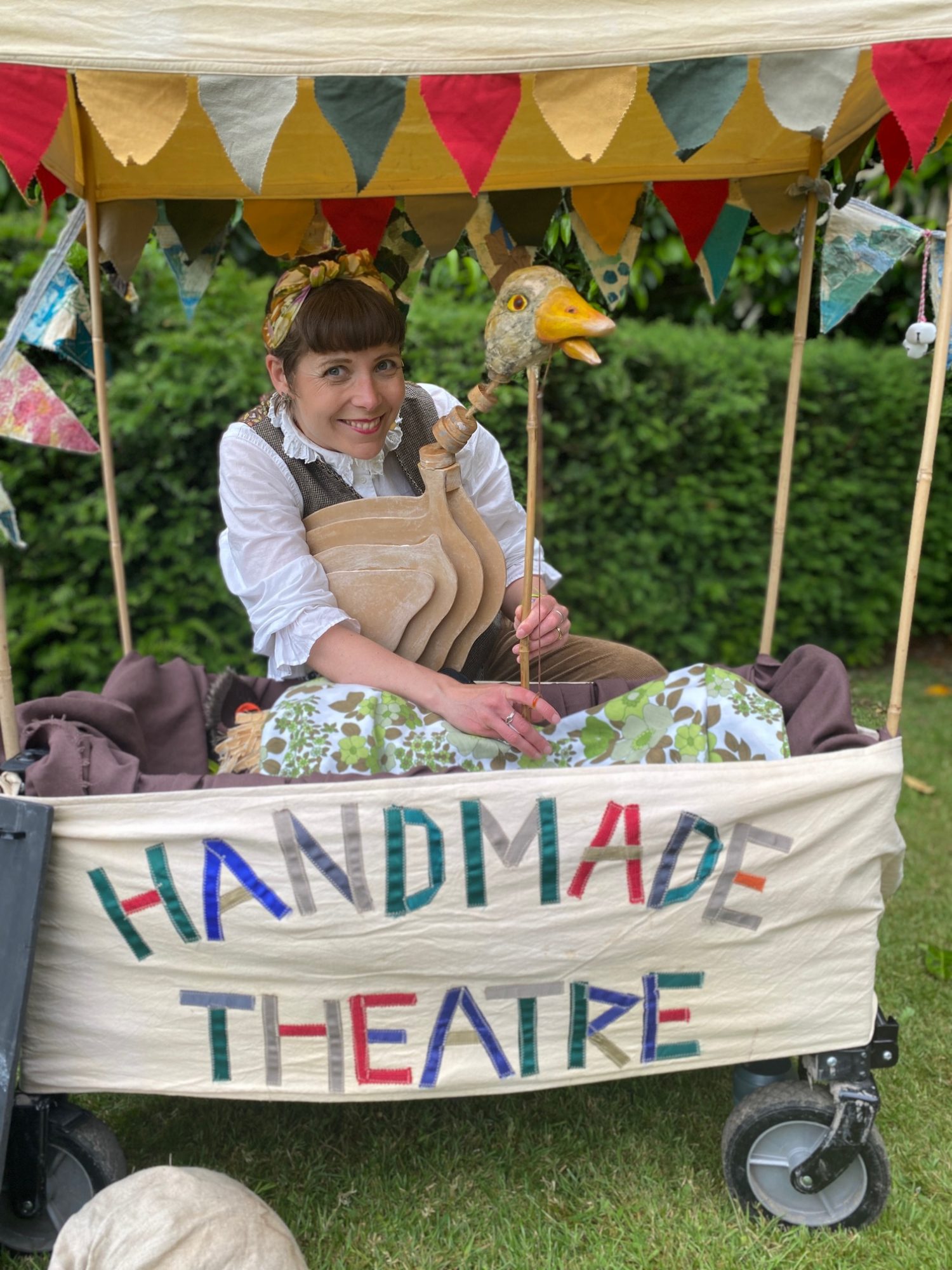 A close-up of a shaggy, handmade highland cow puppet with large horns, being held by a performer in a wooded outdoor setting.